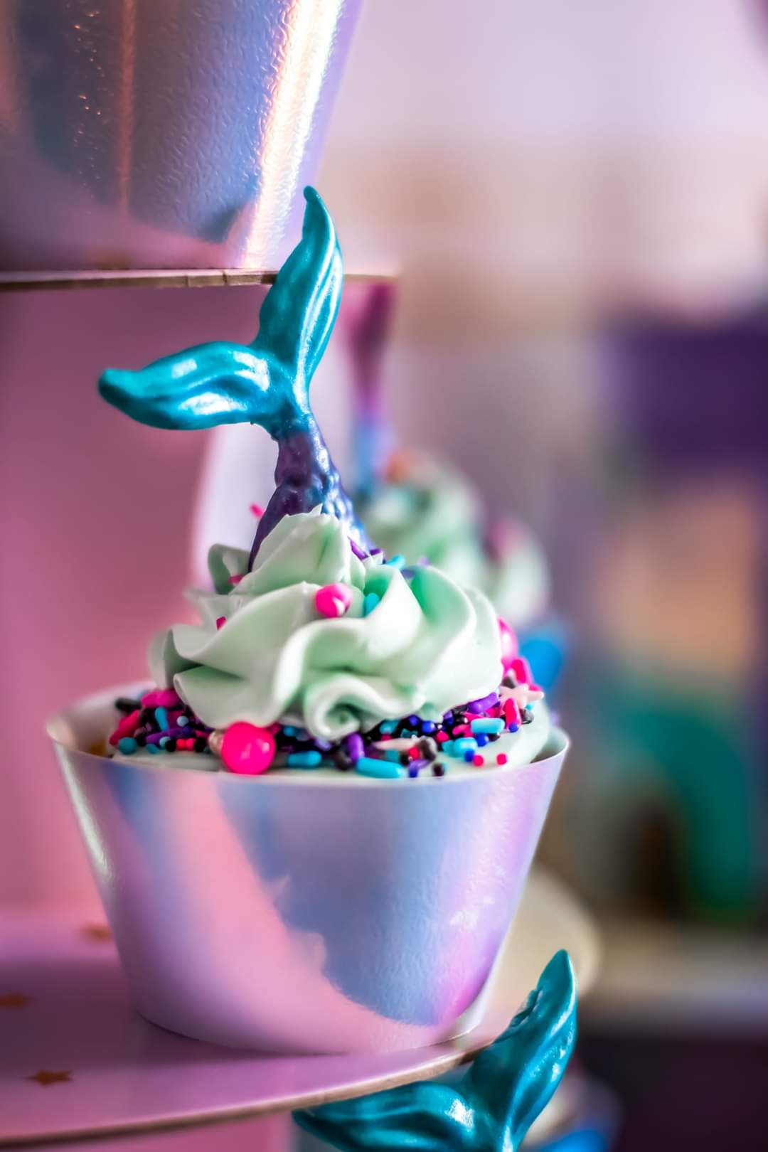 Cupcake with green frosting and colorful sprinkles, featuring a mermaid tail on a pink surface.