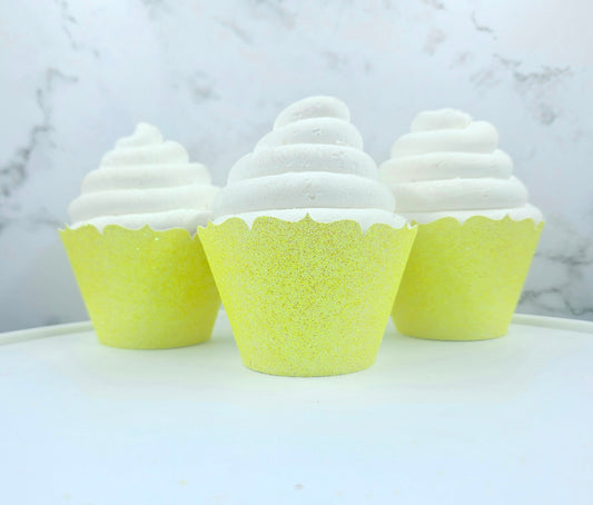 Three cupcakes with white frosting and yellow cupcake liners on a marble surface.